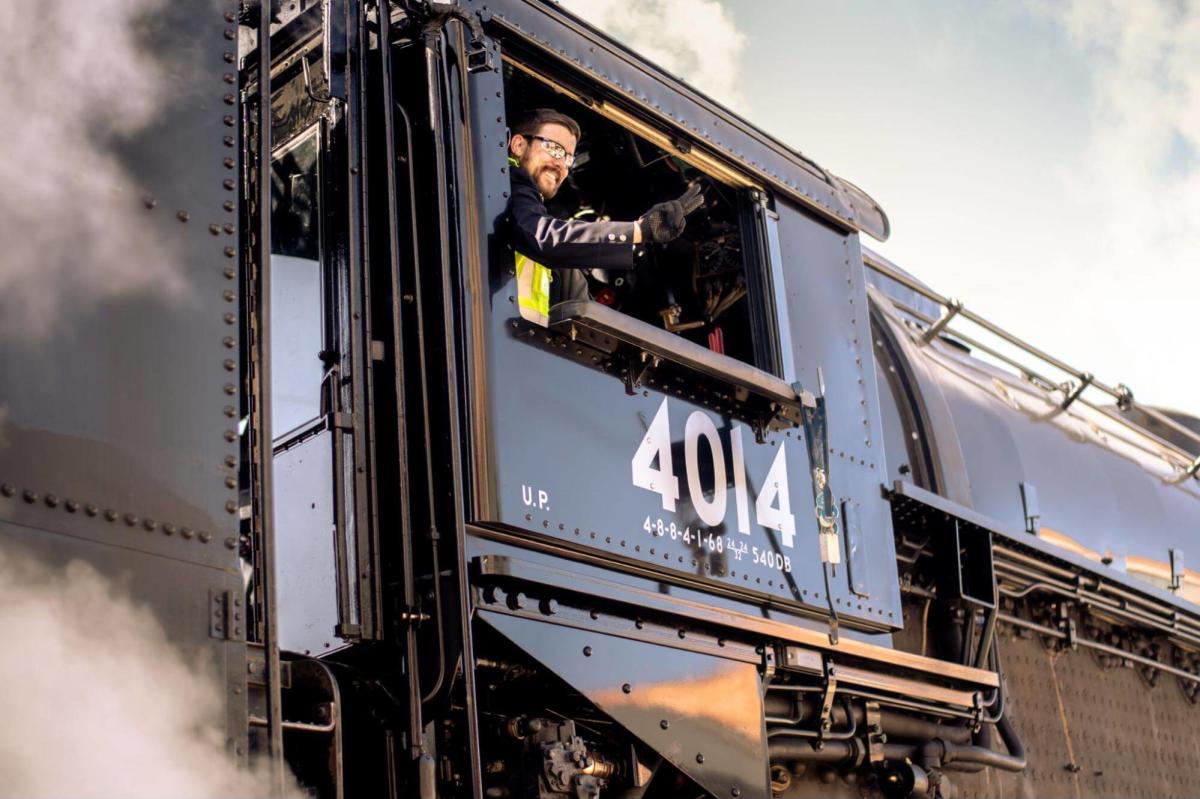 Engineer waving from the cab of the world's biggest train engine, Union Pacific 4014, with steam rising around it.