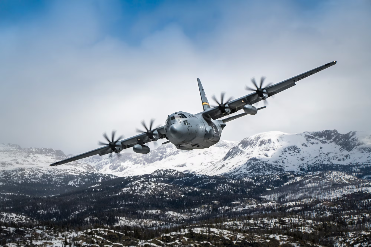 A C-130 Hercules aircraft from the Wyoming Air National Guard's 153rd Airlift Wing flying over a snowy mountain range.