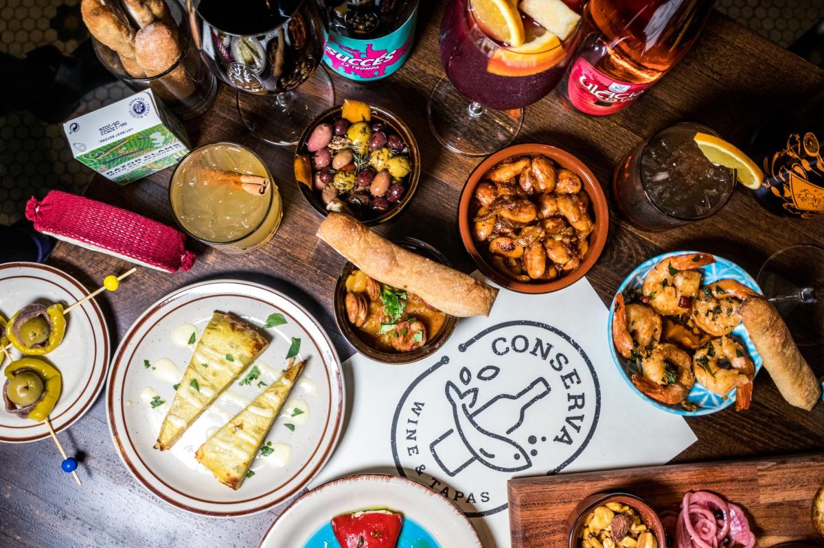 The image is an ariel view of different foods and drinks on a table with a Conserva logo sign.