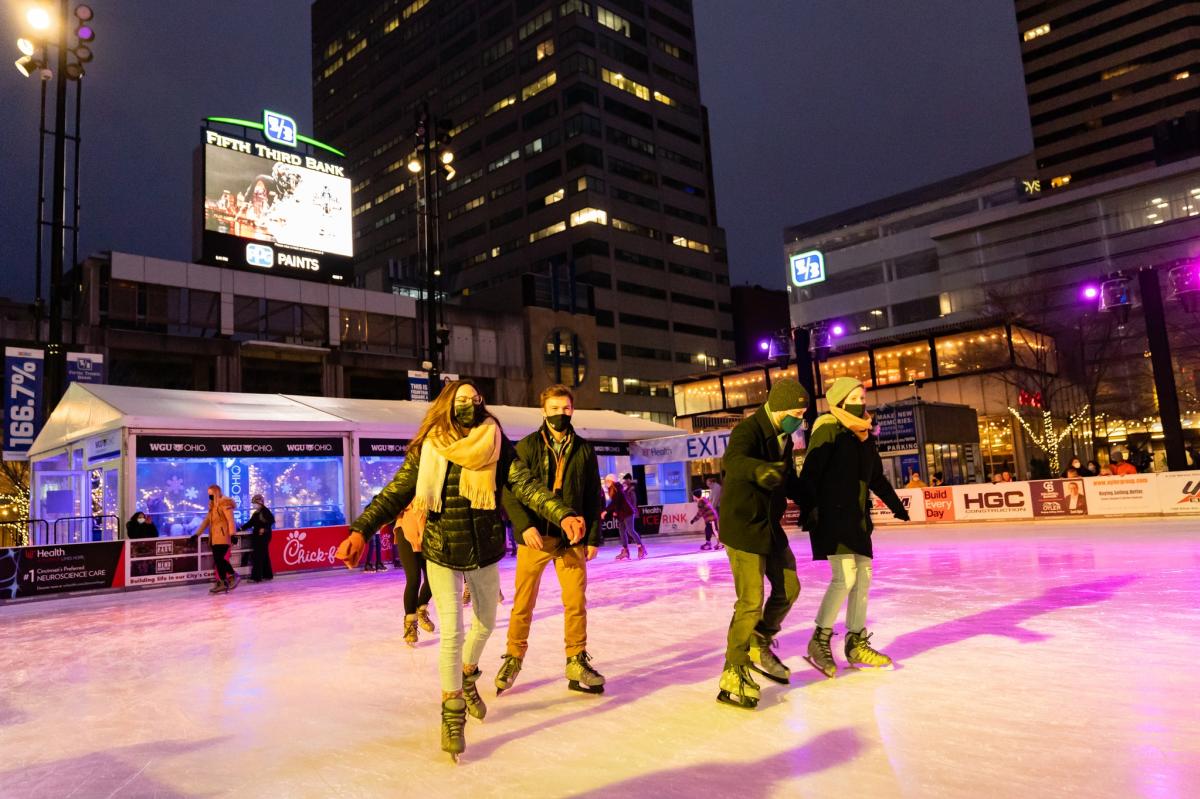 Four people ice skating on Fountain Square's public rink in downtown Cincy