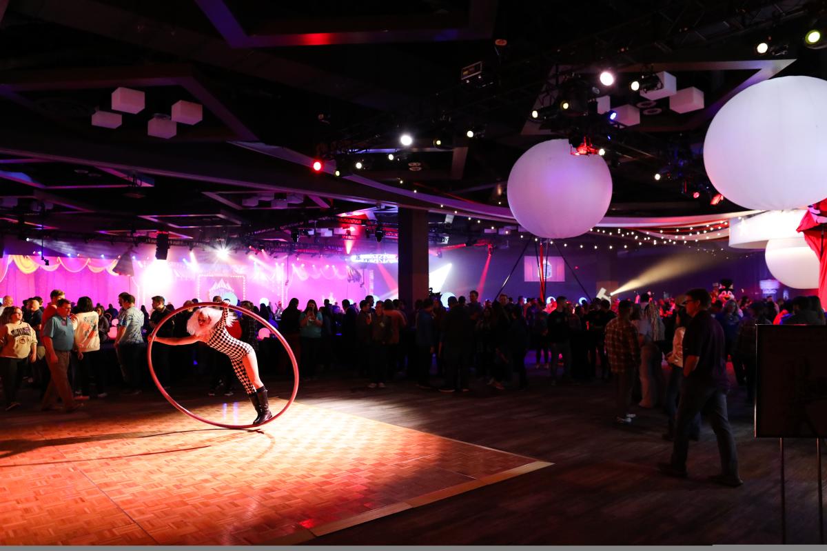 A woman acrobat performs on a ring on the ground with a crowd watching at the Kona Konvention