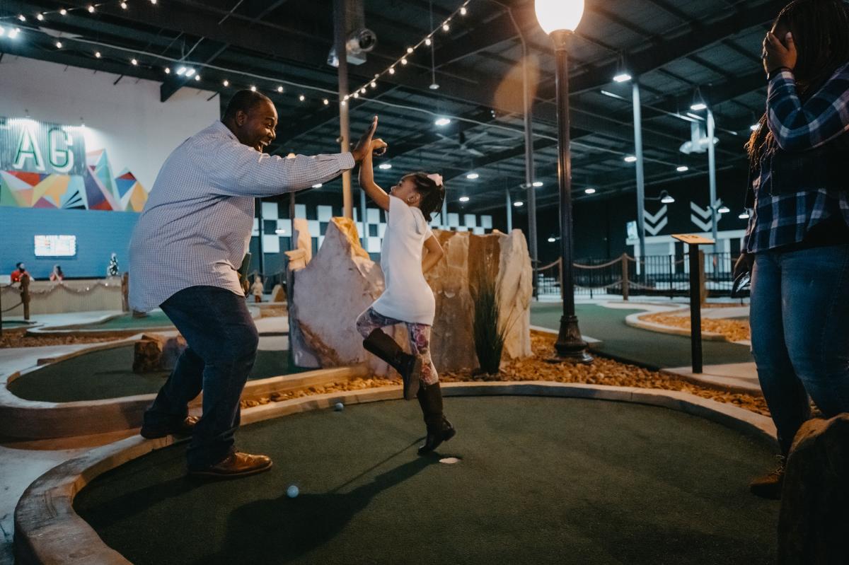 parent and child hi-fiving on an indoor putt-putt course