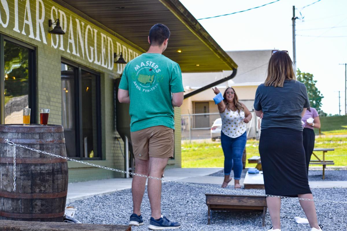 Woman tosses bag onto cornhole board.