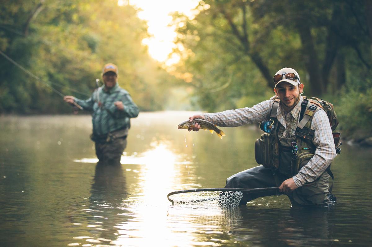 Man Holding Up Caught Fish With Friend in Background in Cumberland Valley