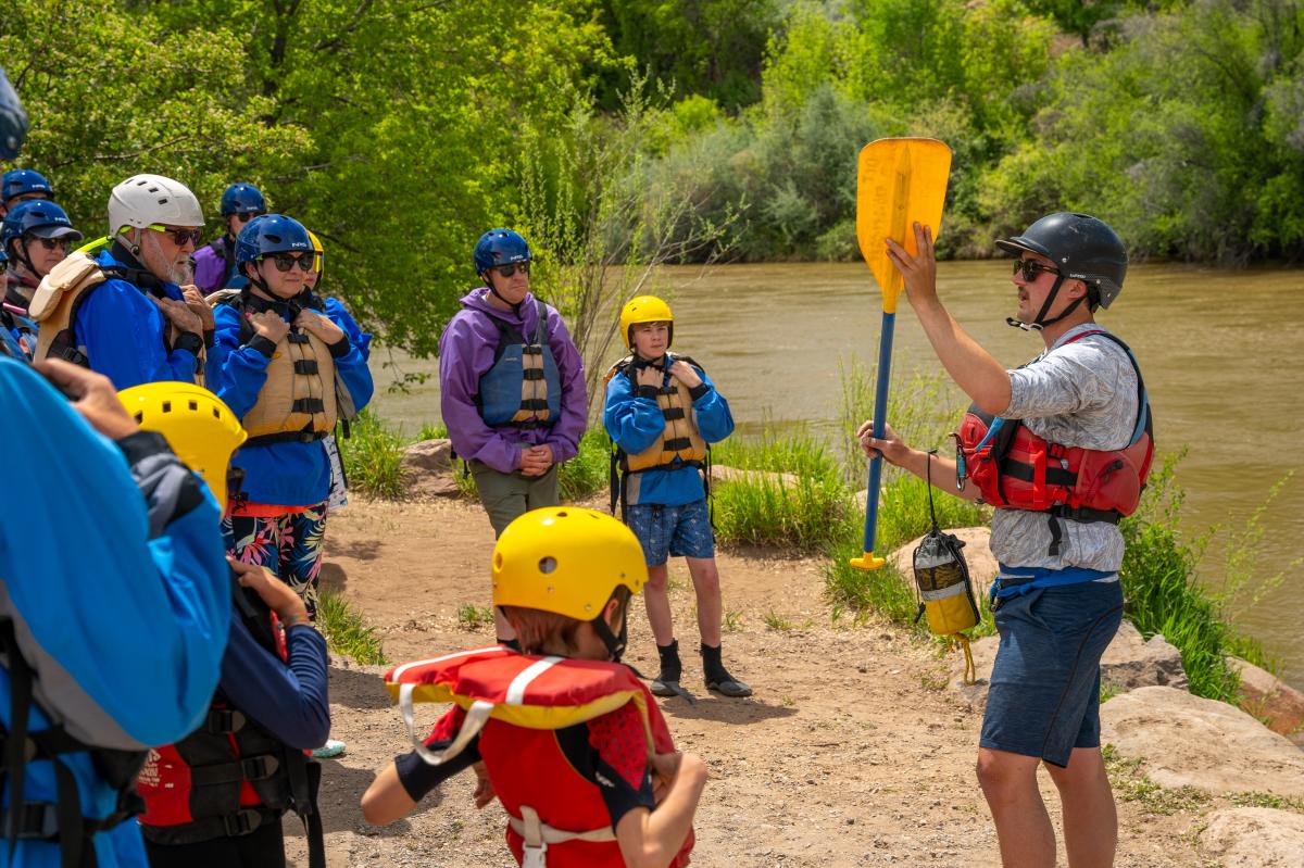 A raft guide giving a paddle tutorial to a group of rafters.