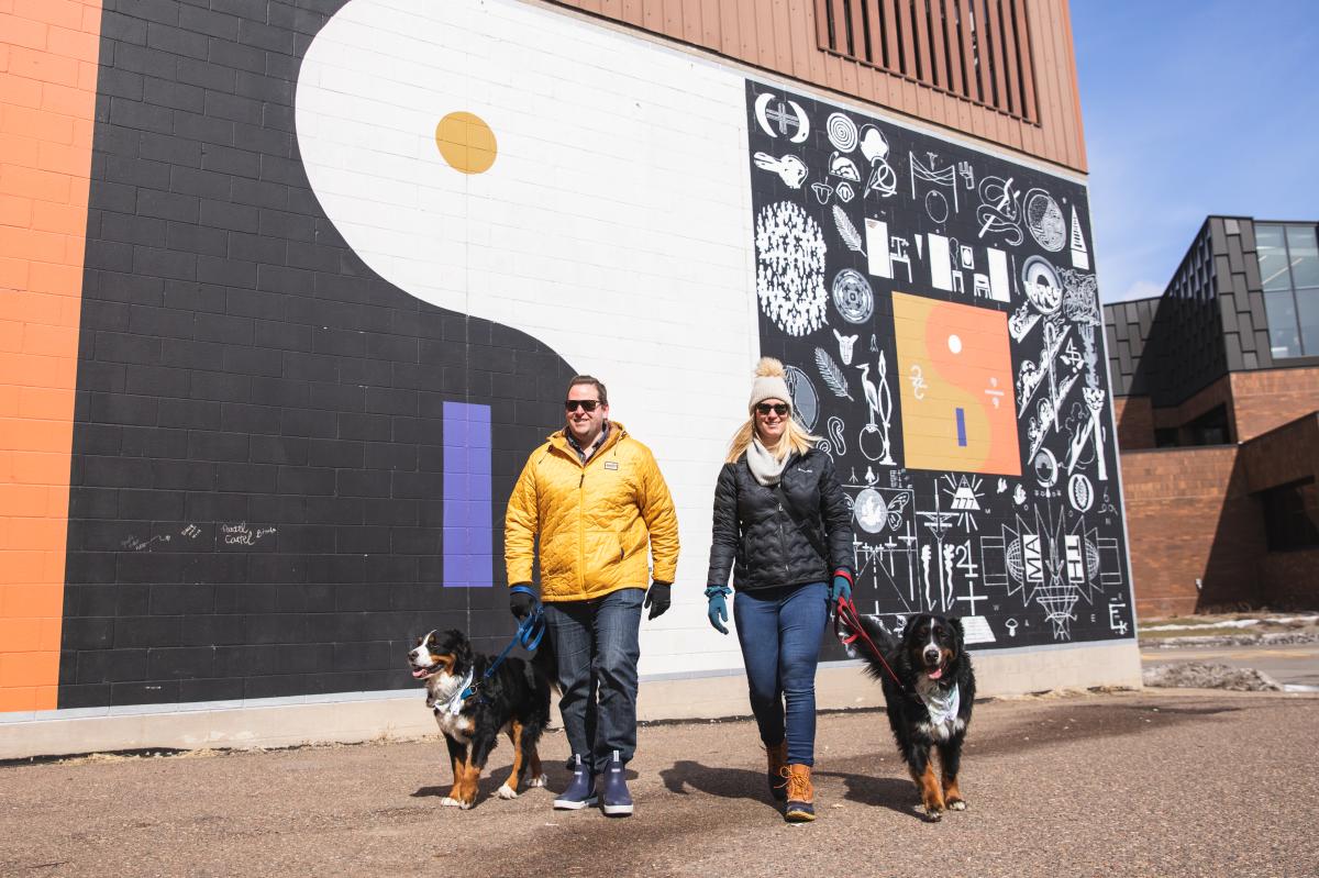 a man and woman walking two dogs in front of the Bon Iver Mural