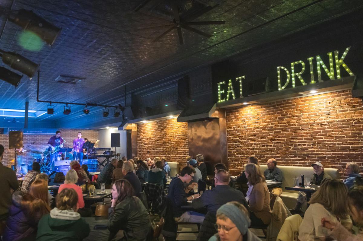 A crowd of people sitting at the tables listening to live music at The Plus