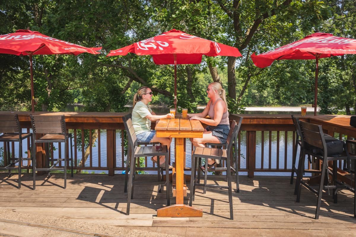 Two girls drinking beer on the patio overlooking the Chippewa River at Loopy's