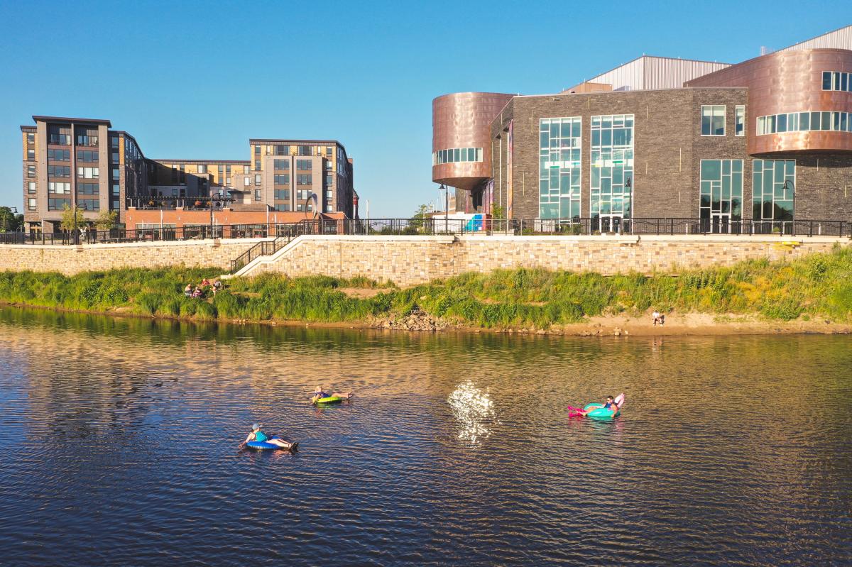 3 people floating on tubes on the Chippewa River in front of the Pablo Center