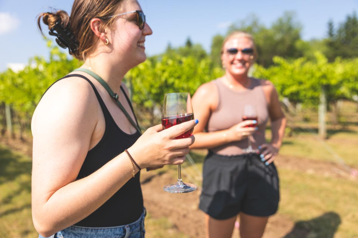 Two girls drinking wine and laughing in the vineyards at River Bend