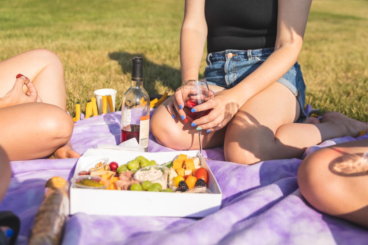A girl holding a glass of wine with a charcuterie board on a blanket in the lawn