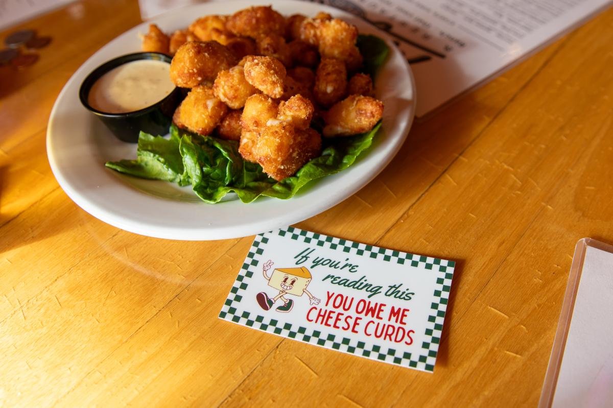 A sticker that says "If you're reading this You owe me cheese curds" next to a plate of cheese curds