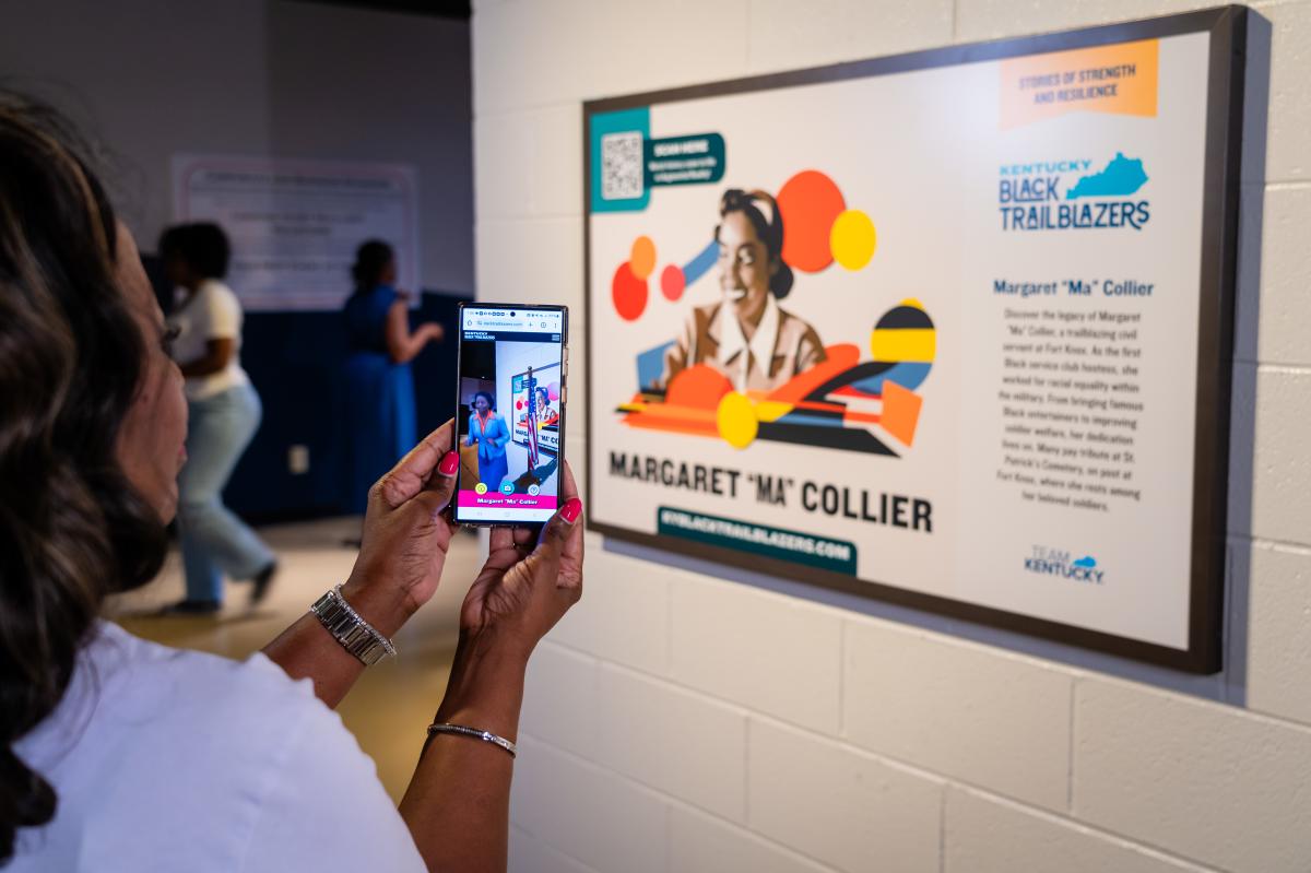 A woman takes a photo of an exhibit featuring Margaret "Ma" Collier at the Kentucky Black Trailblazers display.