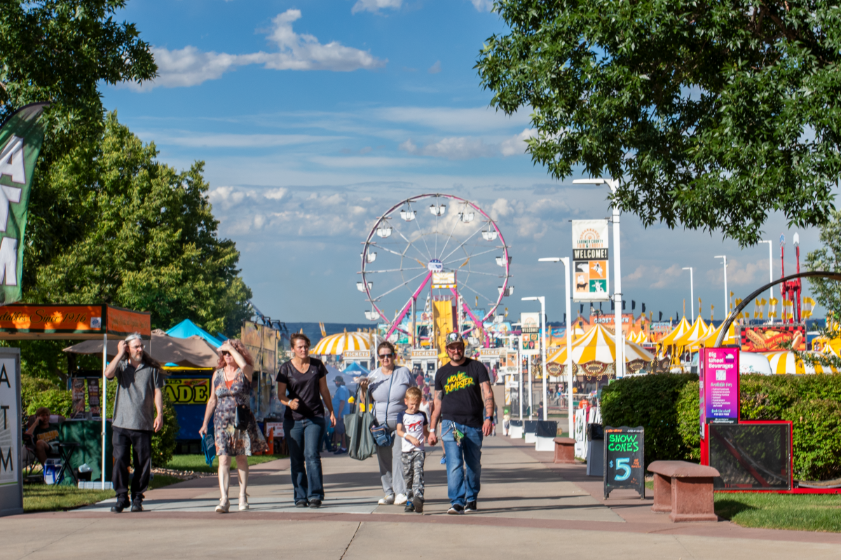 family walks down path at county fair with carnival rides and tents in the background
