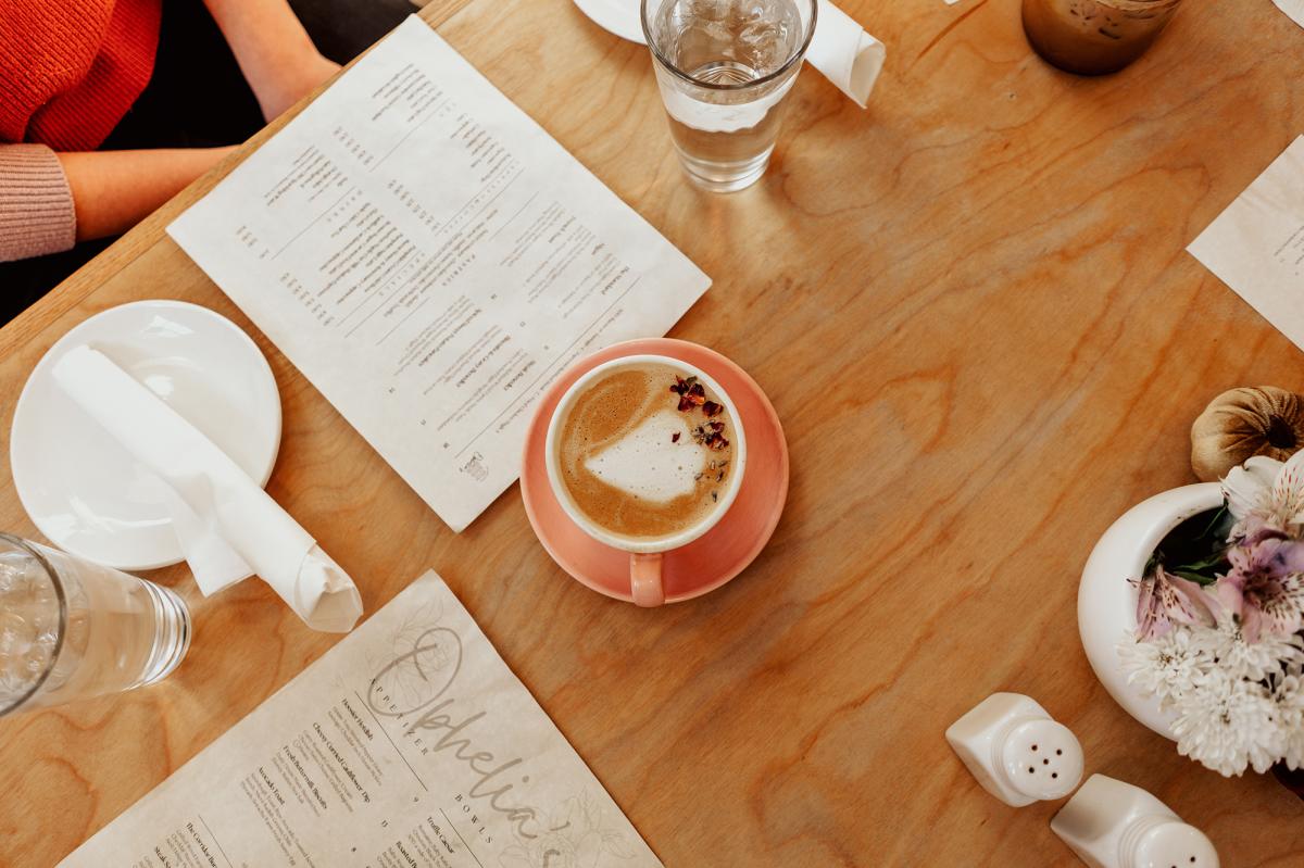 a coffee mug filled with a latte sits on a wooden tabletop next to menus
