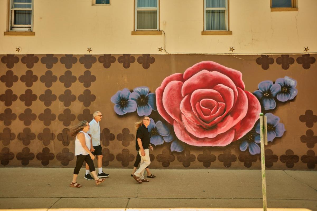 Four people walking on a sidewalk, in front of a mural of flowers.