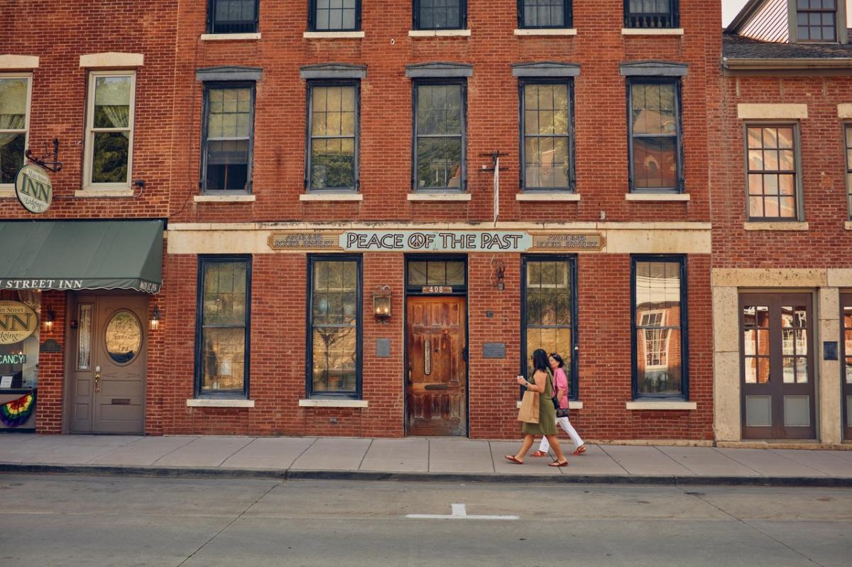 Two people walking along a red brick building. The building says, "Peace of the Past."