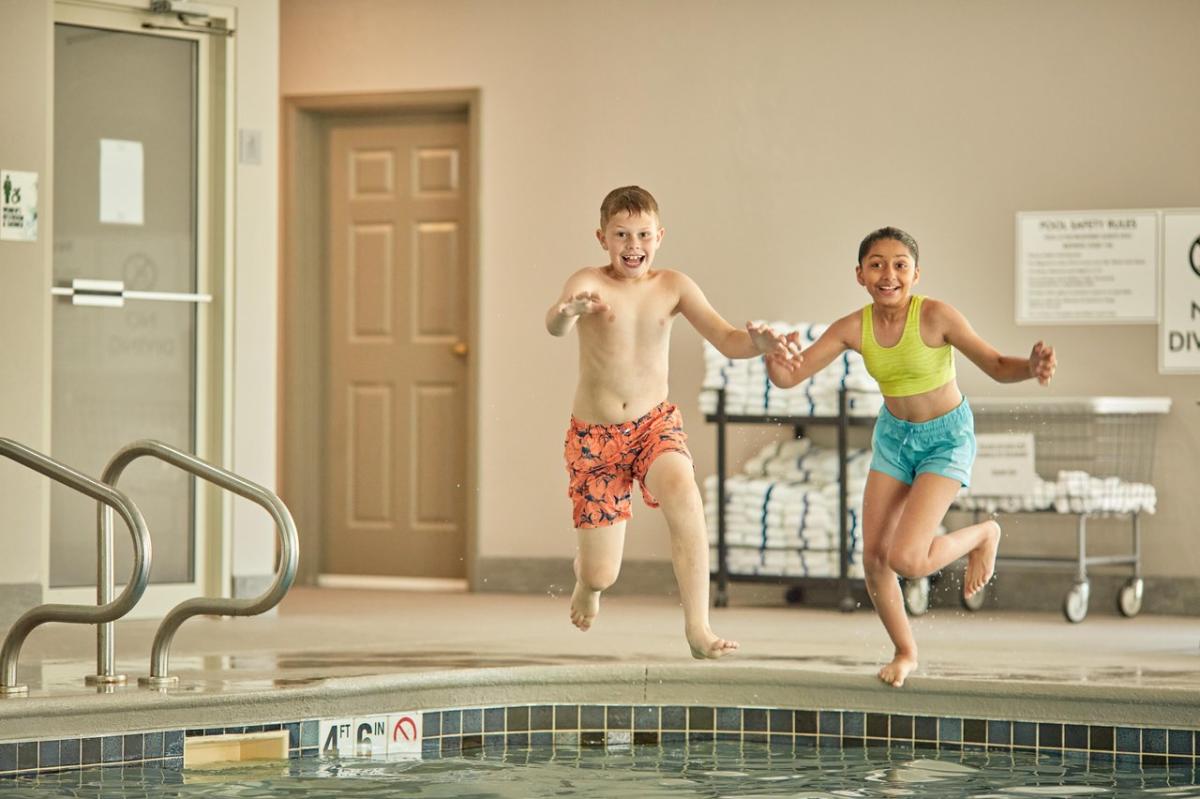 Two kids jumping in an indoor swimming pool.