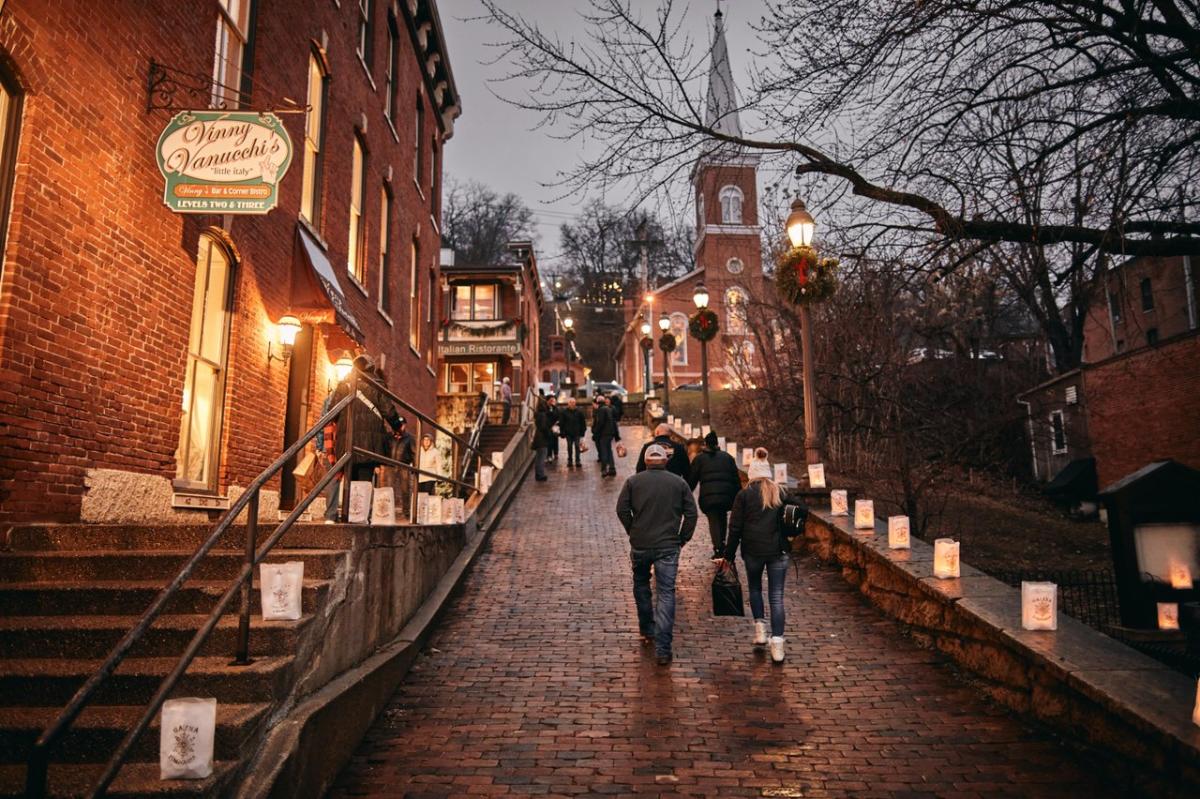 Nighttime, looking up a brick walkway lined with luminaries, and a steeple in the background.