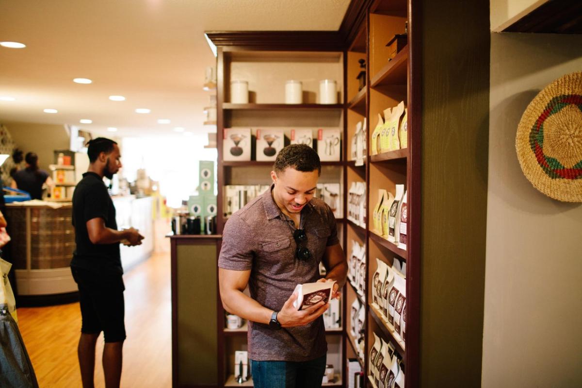 A person holding a bag of coffee and reading the label. Another person is shopping behind them.