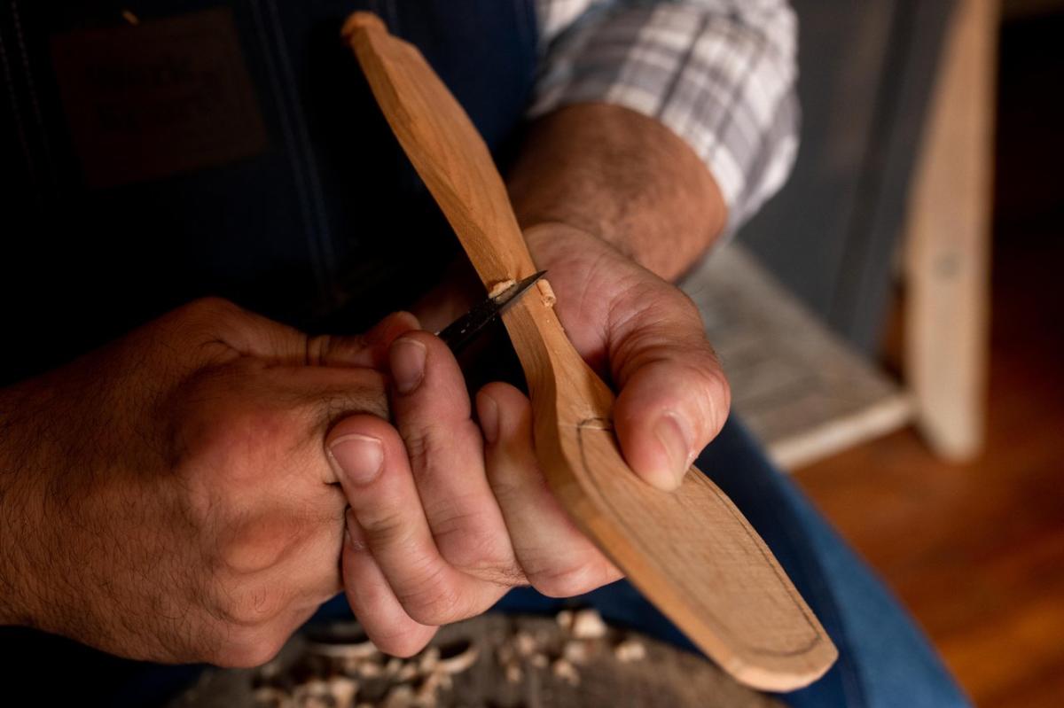 Person holding a utensil that they're carving out of wood.