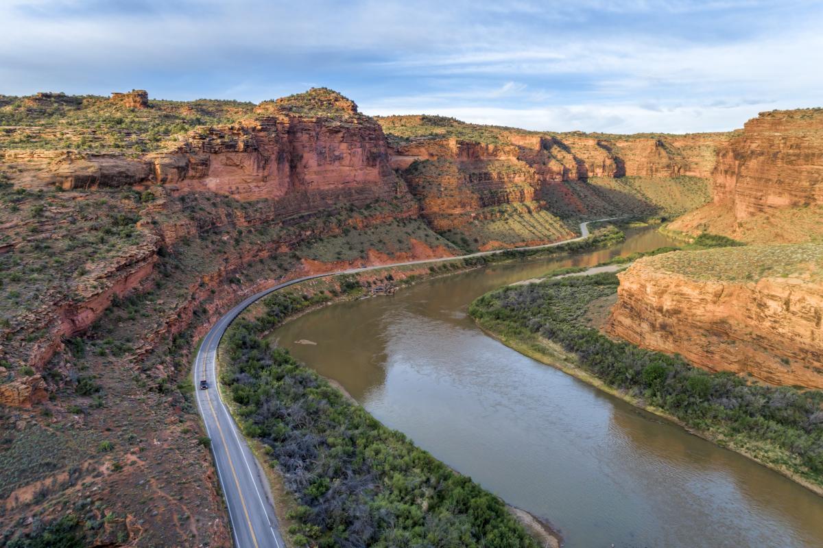 An aerial view of the Upper Colorado River Scenic Byway (Utah State Route 128) winding alongside the Colorado River through a dramatic red rock canyon near Moab, Utah.