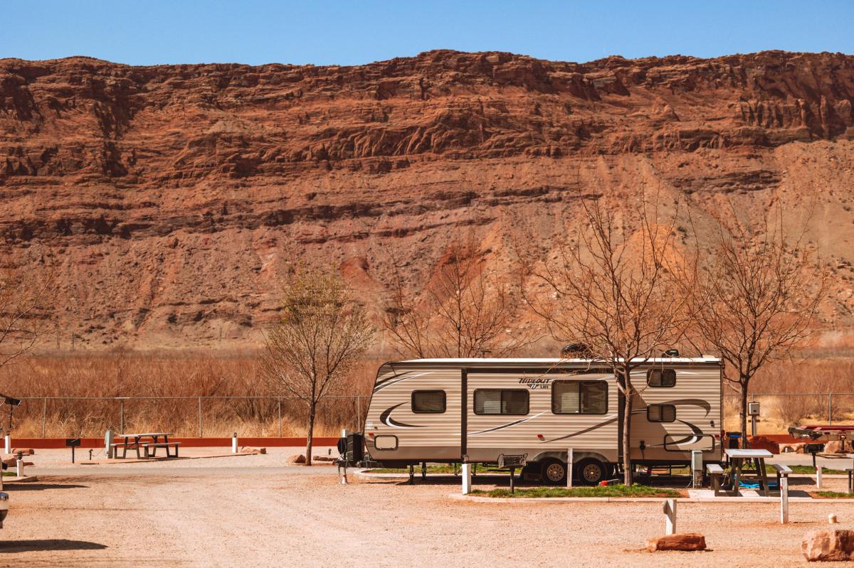 RV parked beneath towering red rock cliffs at a scenic campground near Moab.