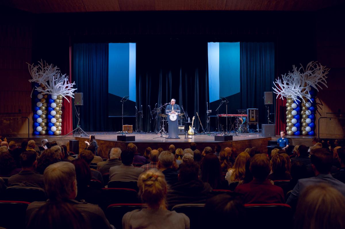 Mayor John Gates stands behind podium during the 2025 State of the City address before a crowd on attendees.