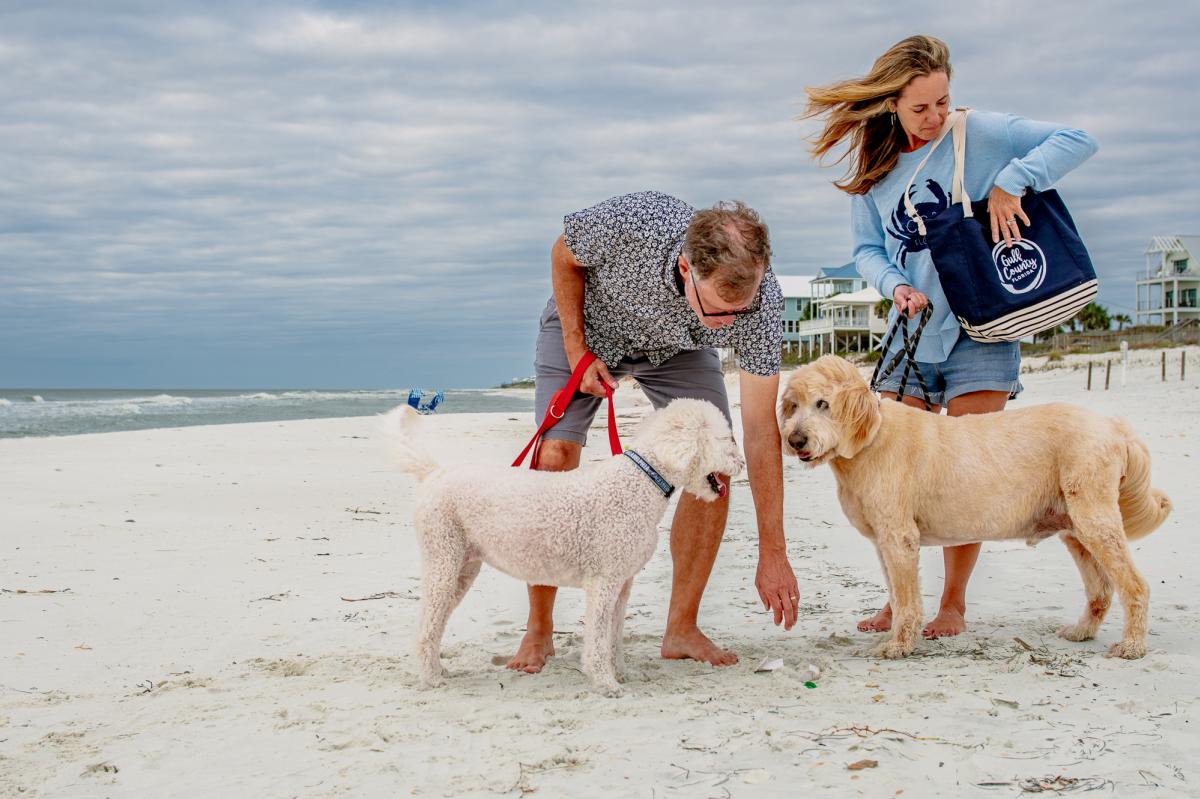 A couple picks up trash while walking the beach with their dogs.