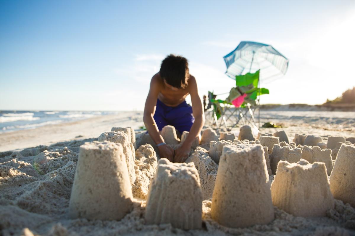 A young boy digs in the sand and builds sandcastles on a white sand beach