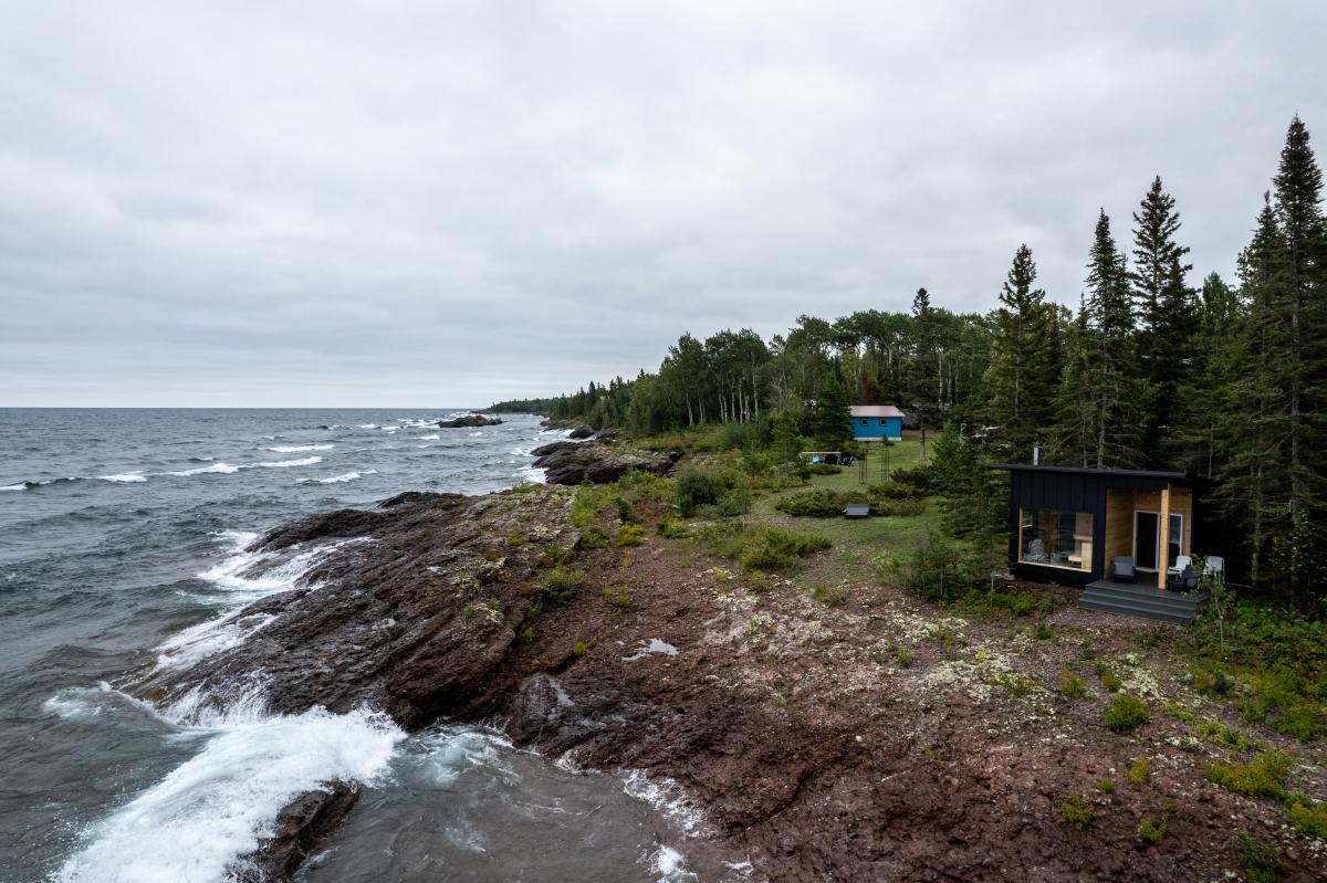 a sauna sits between and forest and rocky lakeshore
