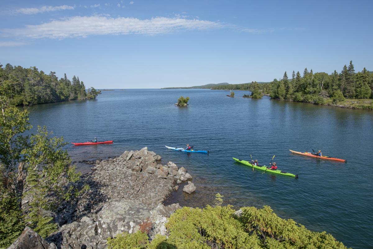 Group of 4 colorful kayaks kayak around rocky shoreline in Copper Harbor.