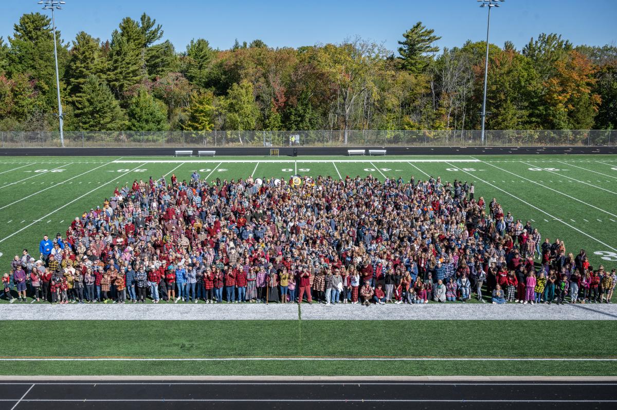 hundreds of people dressed in plaid pack a football field