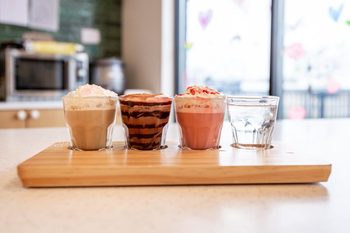 A wooden board holding a coffee flight with three coffee drinks and a cup of water.