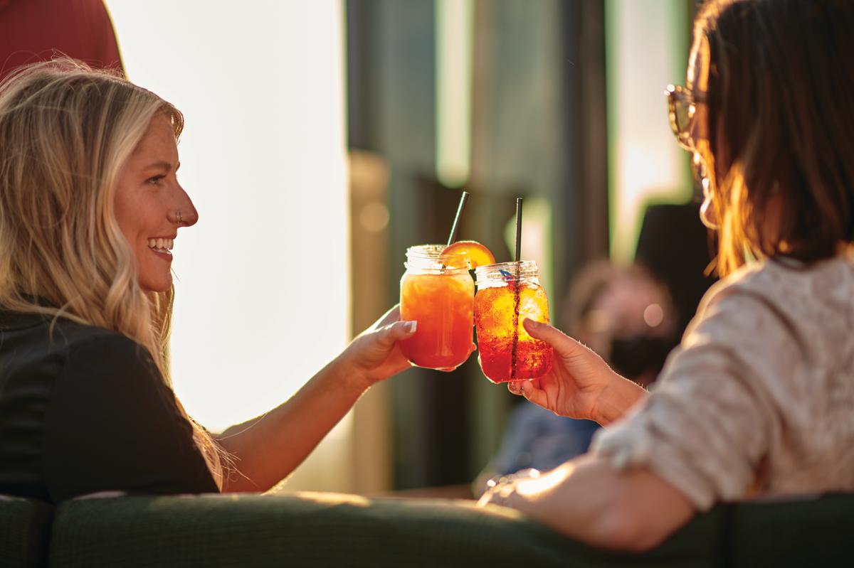 Two women clink their cocktails together at sunset.