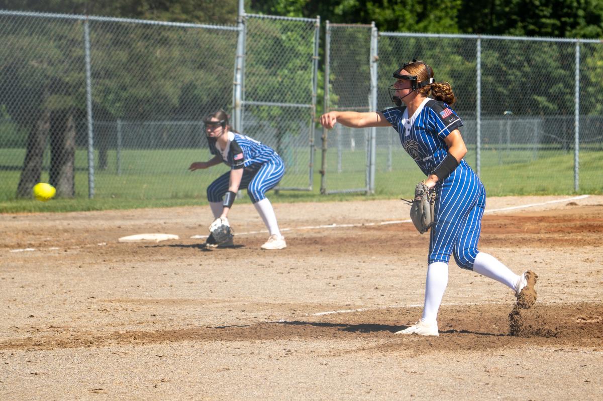 A pitcher throwing the softball with a player on 3rd base