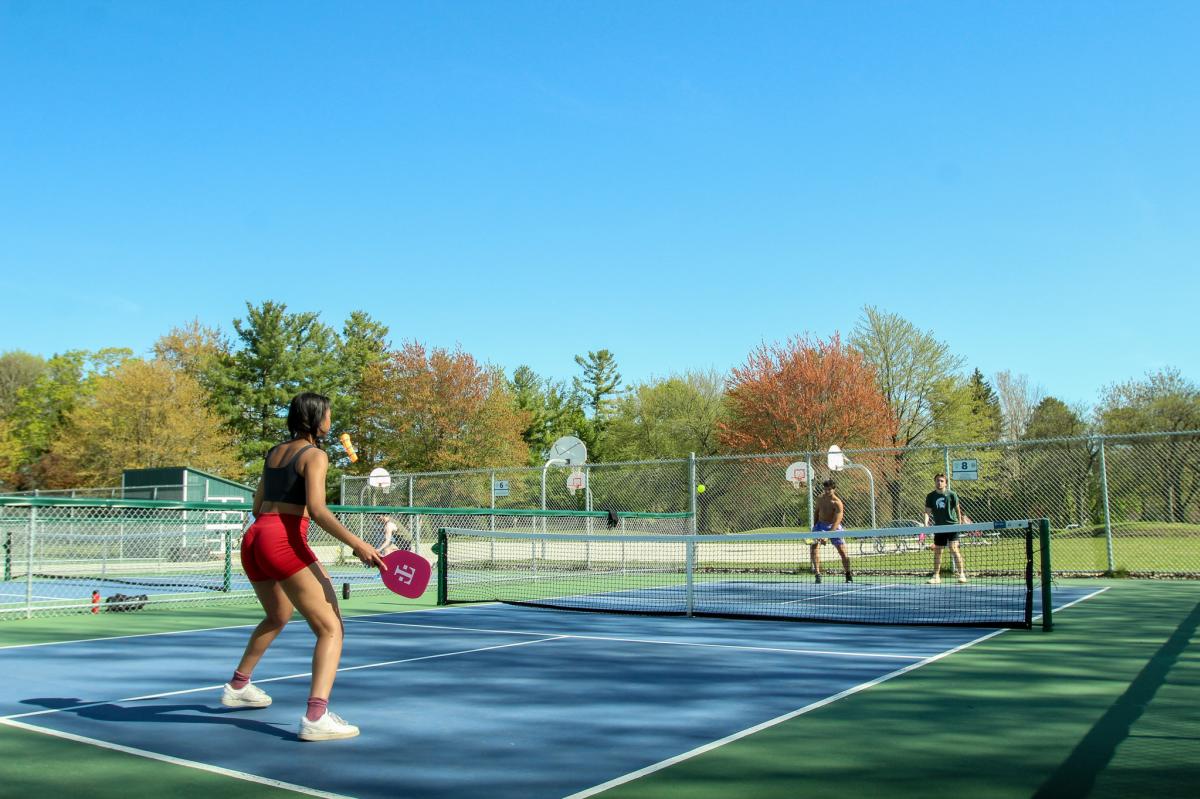 People playing pickleball in an outdoor court under a blue sky.