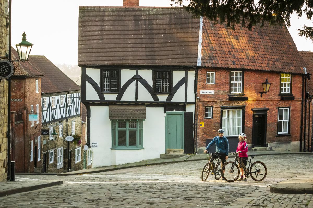 A couple of cyclists stood with bikes on the cobbled streets of Lincoln's Steep Hill.