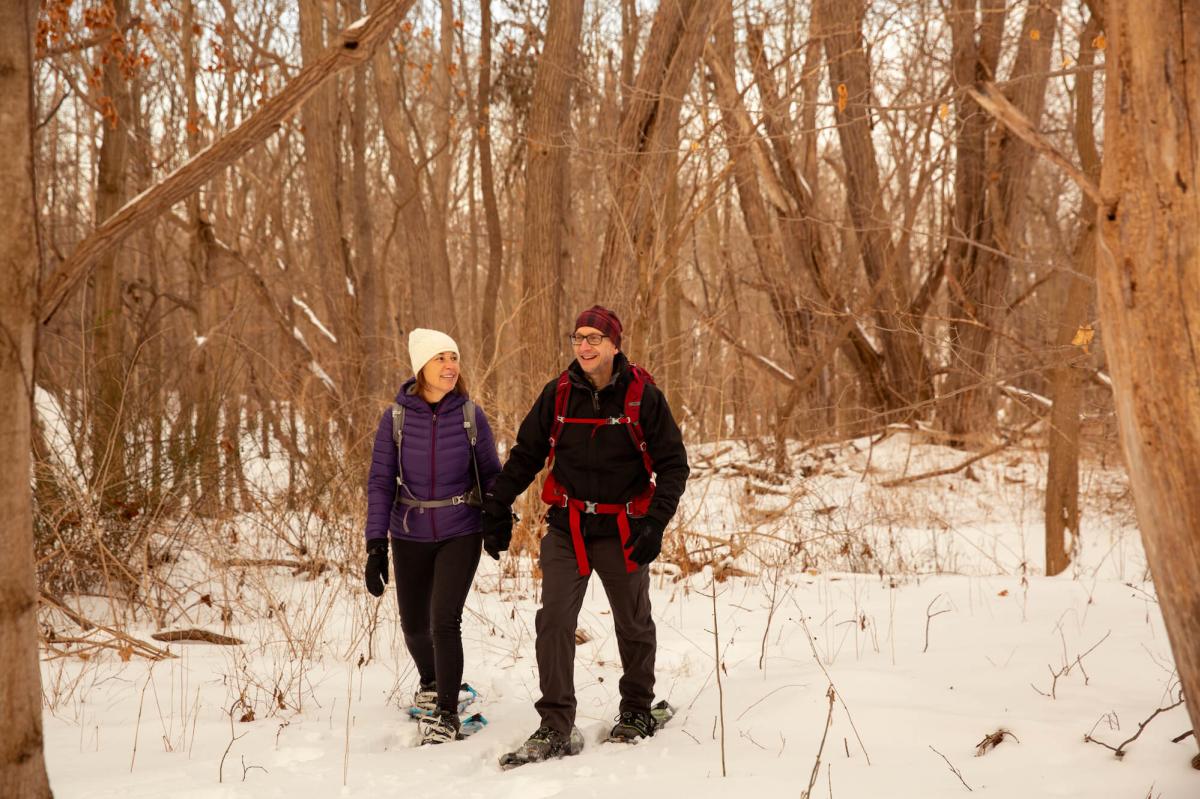 Man and woman snowshoeing through woods