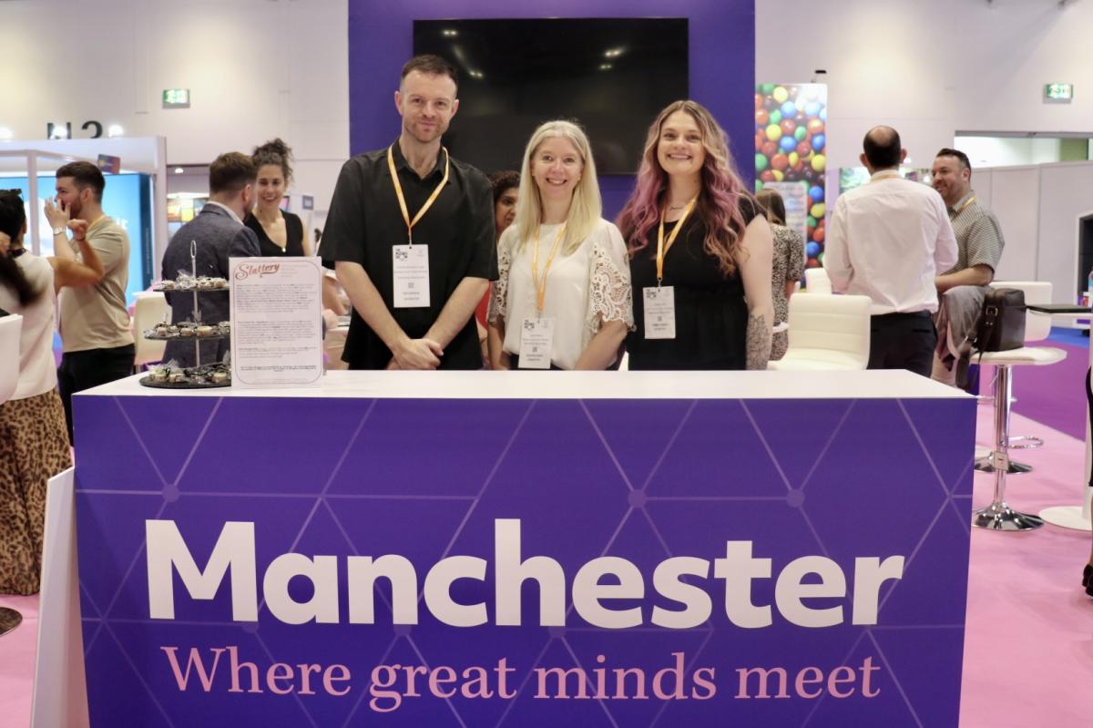 Three representatives stand behind the Manchester exhibition stand at The Meetings Show 2026, with the slogan "Manchester – Where great minds meet" displayed prominently on the front.