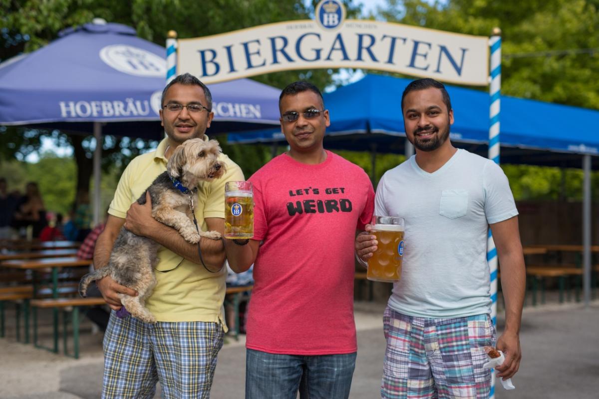 Three men and a dog at the Estabrook Beer Garden, smiling and holding steins of beer.