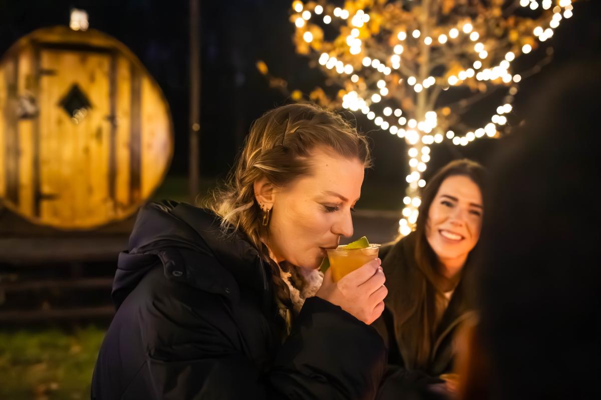 A woman sips a mocktail with twinkly lights in the background