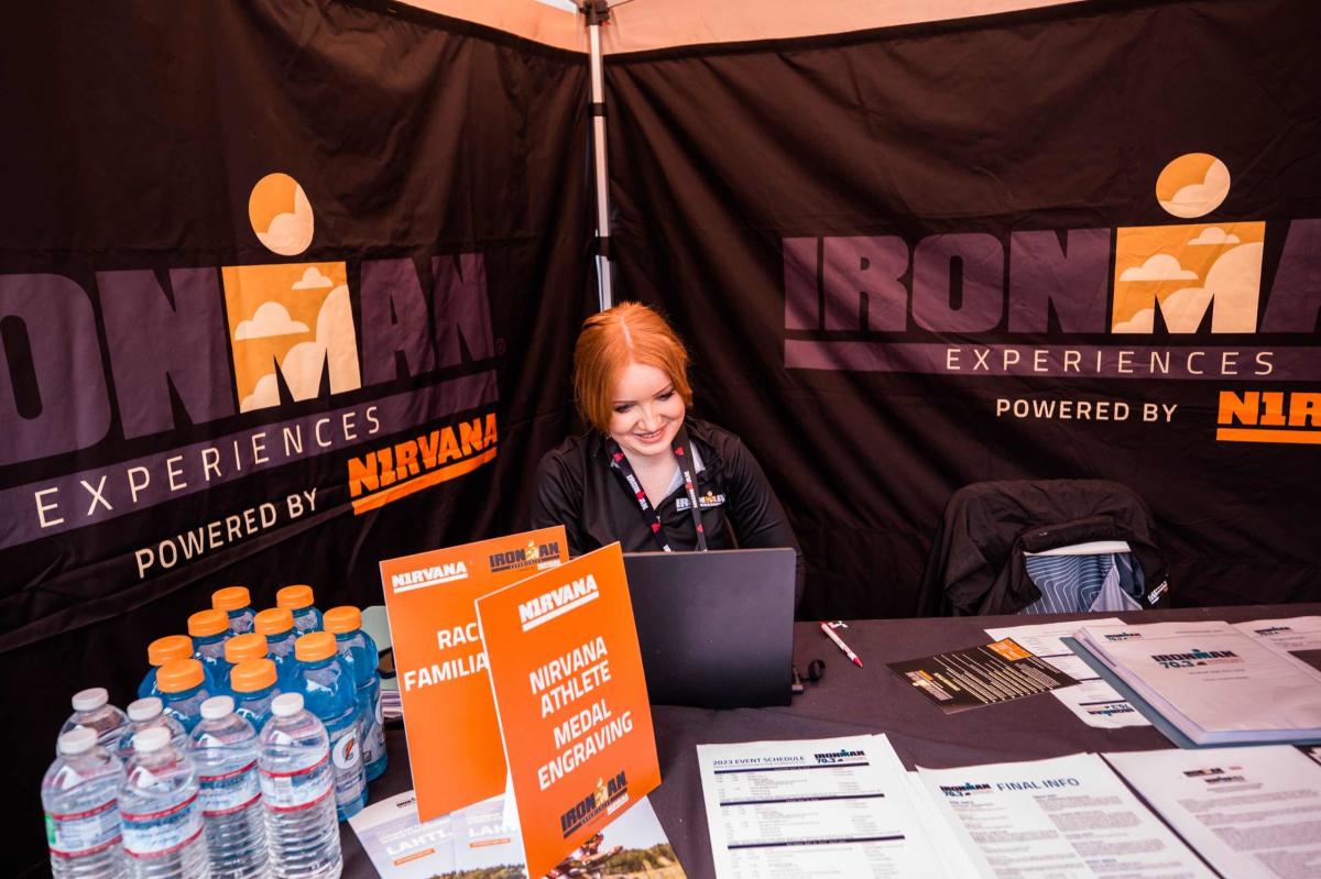 An IRONMAN volunteer sits behind a race registration/check-in desk.