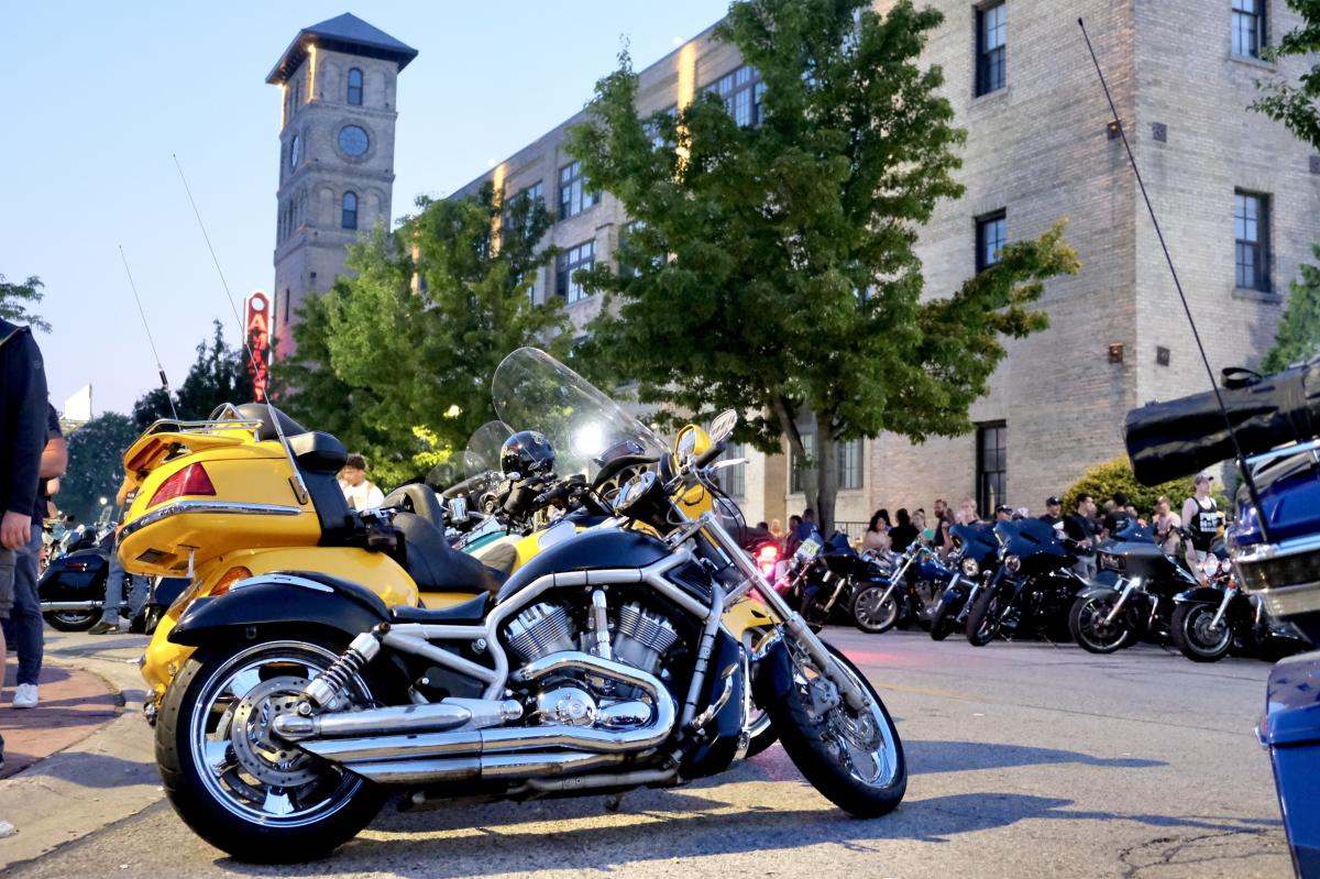 Motorcycles parked on a city street at dusk with a historic tower building in the background.