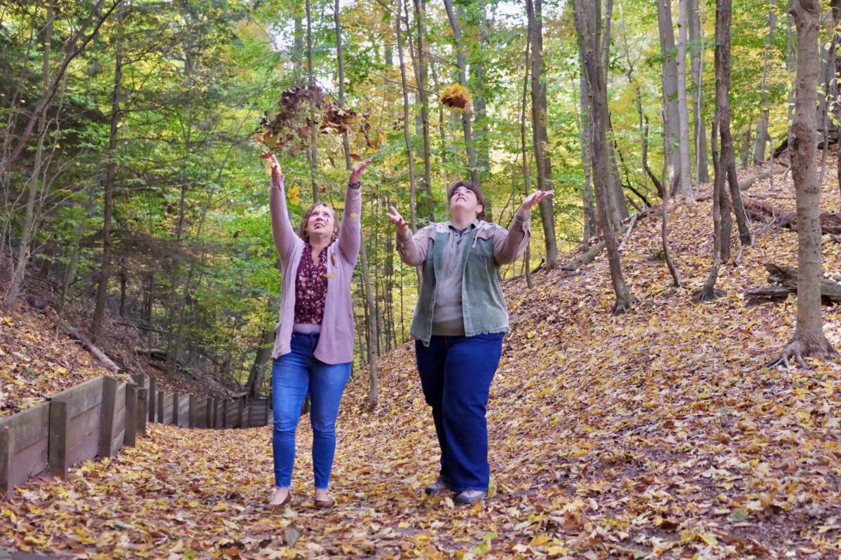 Two people walking on a wooden trail in a forest during autumn.