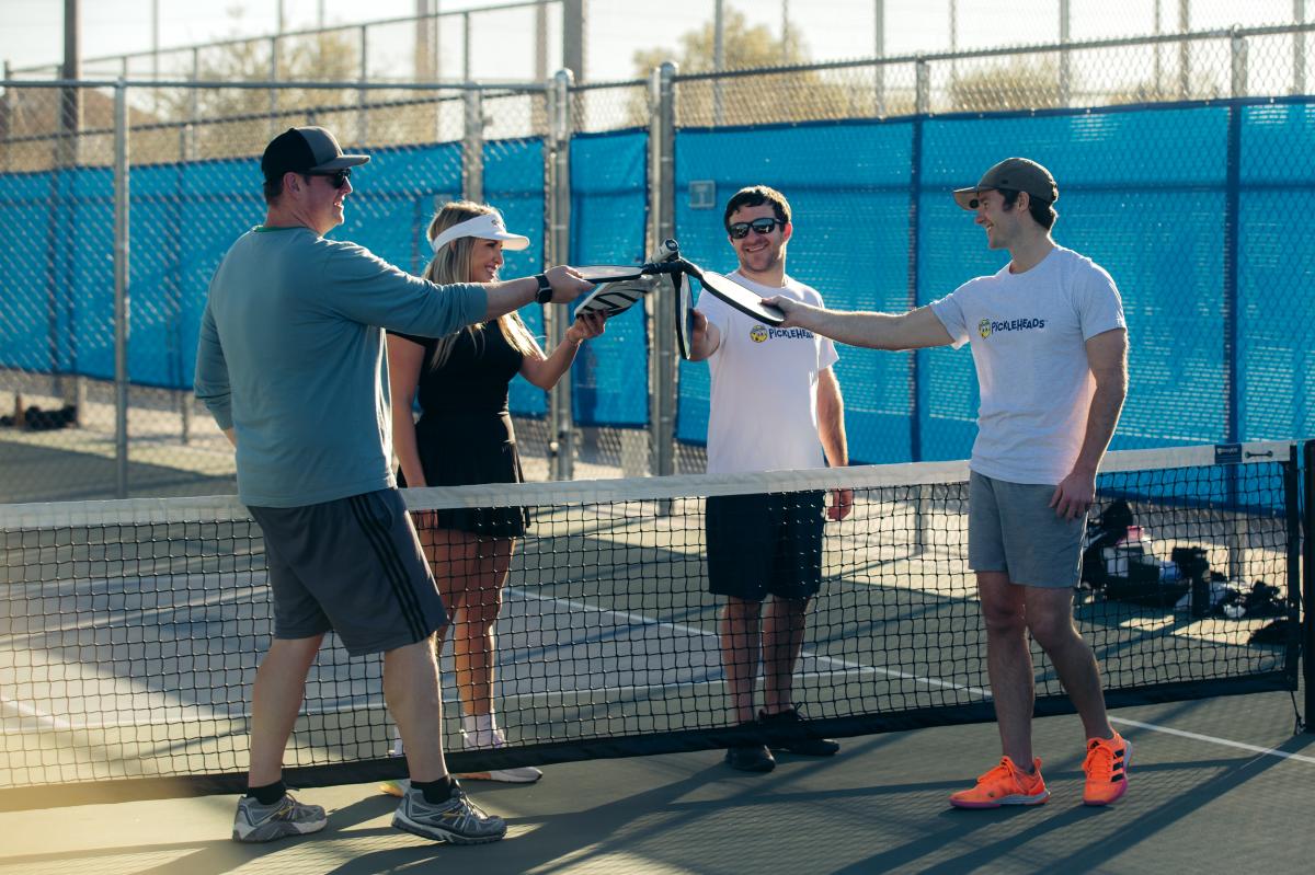 four players on pickleball court touch paddles over net