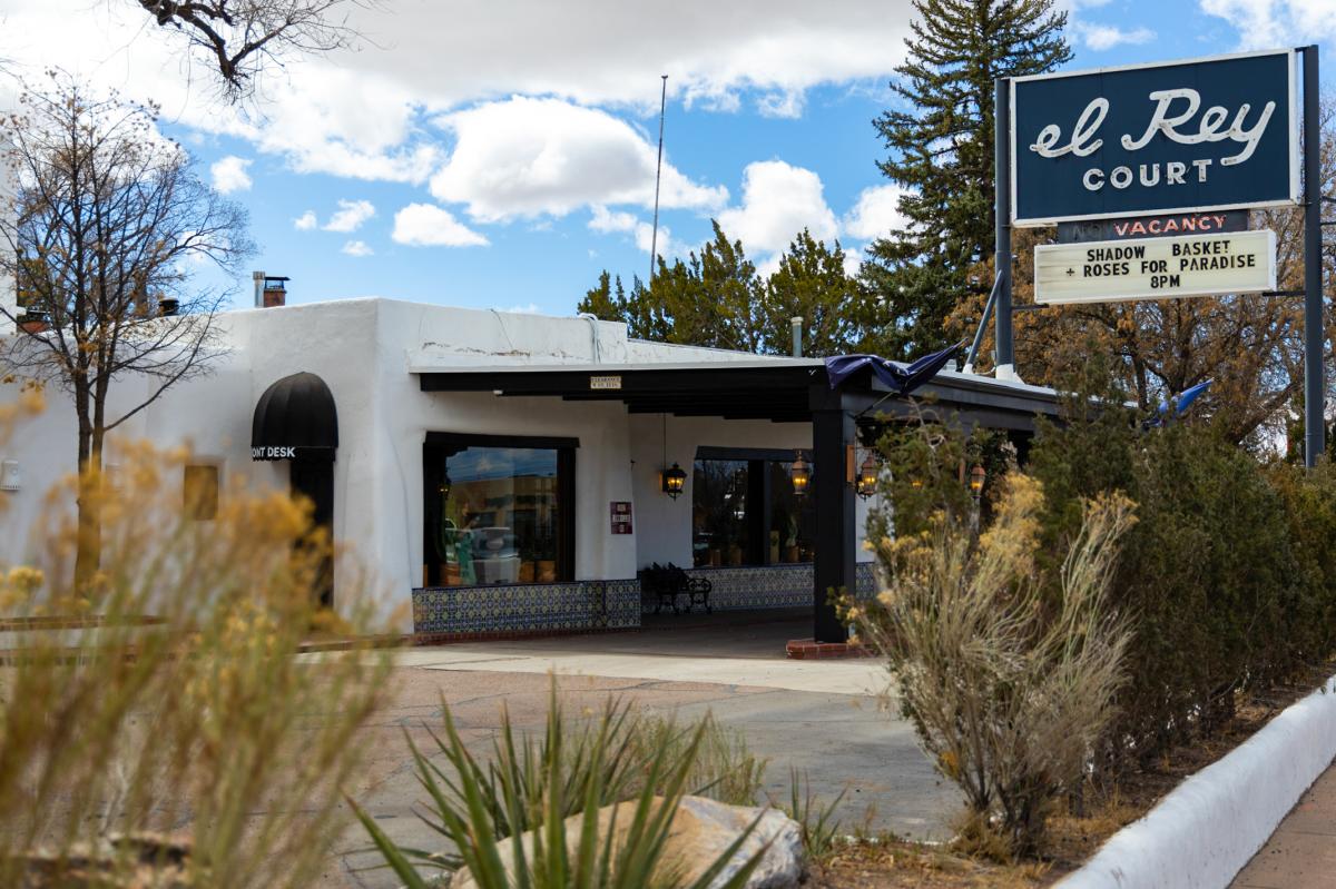 Exterior view of El Rey Court, featuring a vintage-style motel with a white stucco building, decorative tiles, and a retro blue sign advertising vacancy.
