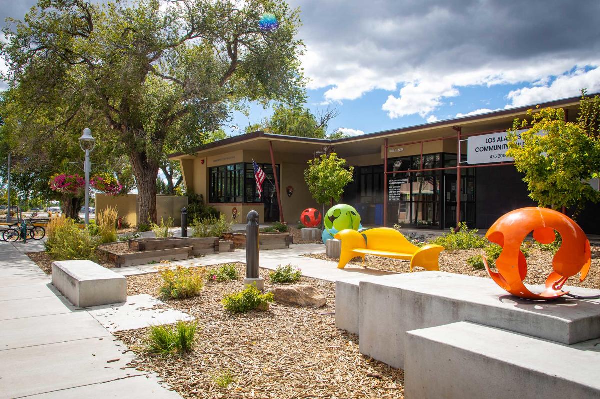 Exterior of a building with concrete benches and colorful sculptures with trees and plants scattered around
