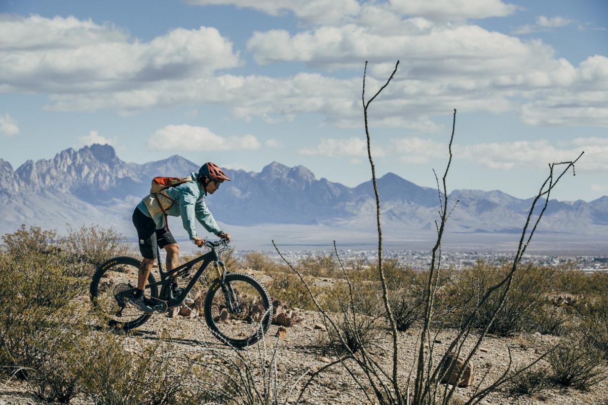 Person riding a mountain bike on a desert trail with rugged mountains in the background.