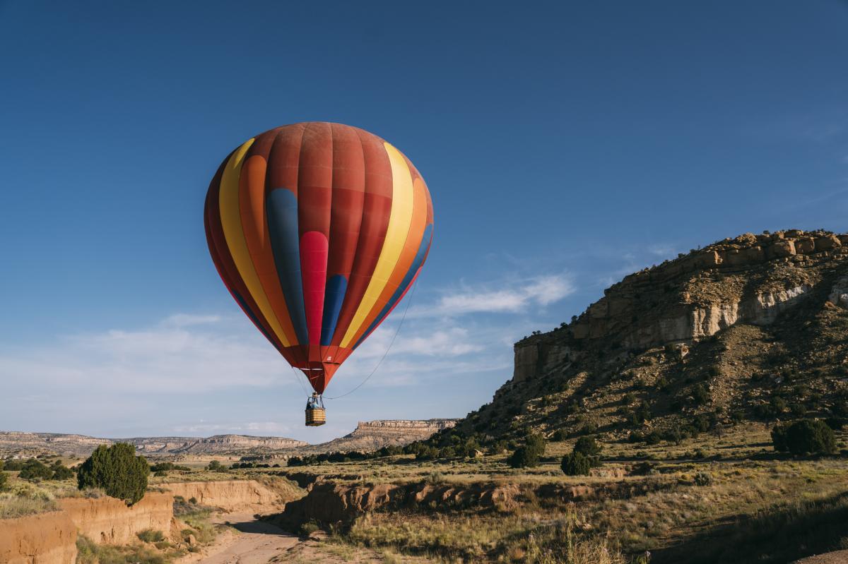 A colorful hot air balloon floats in a clear blue sky above a rugged landscape with rock formations.